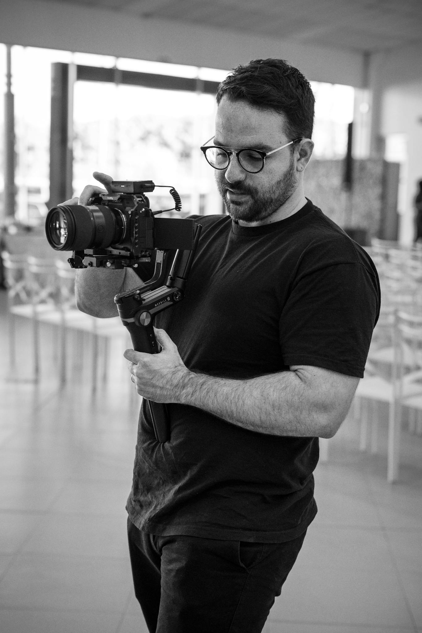 A black and white image capturing a filmmaker with a camera indoors.