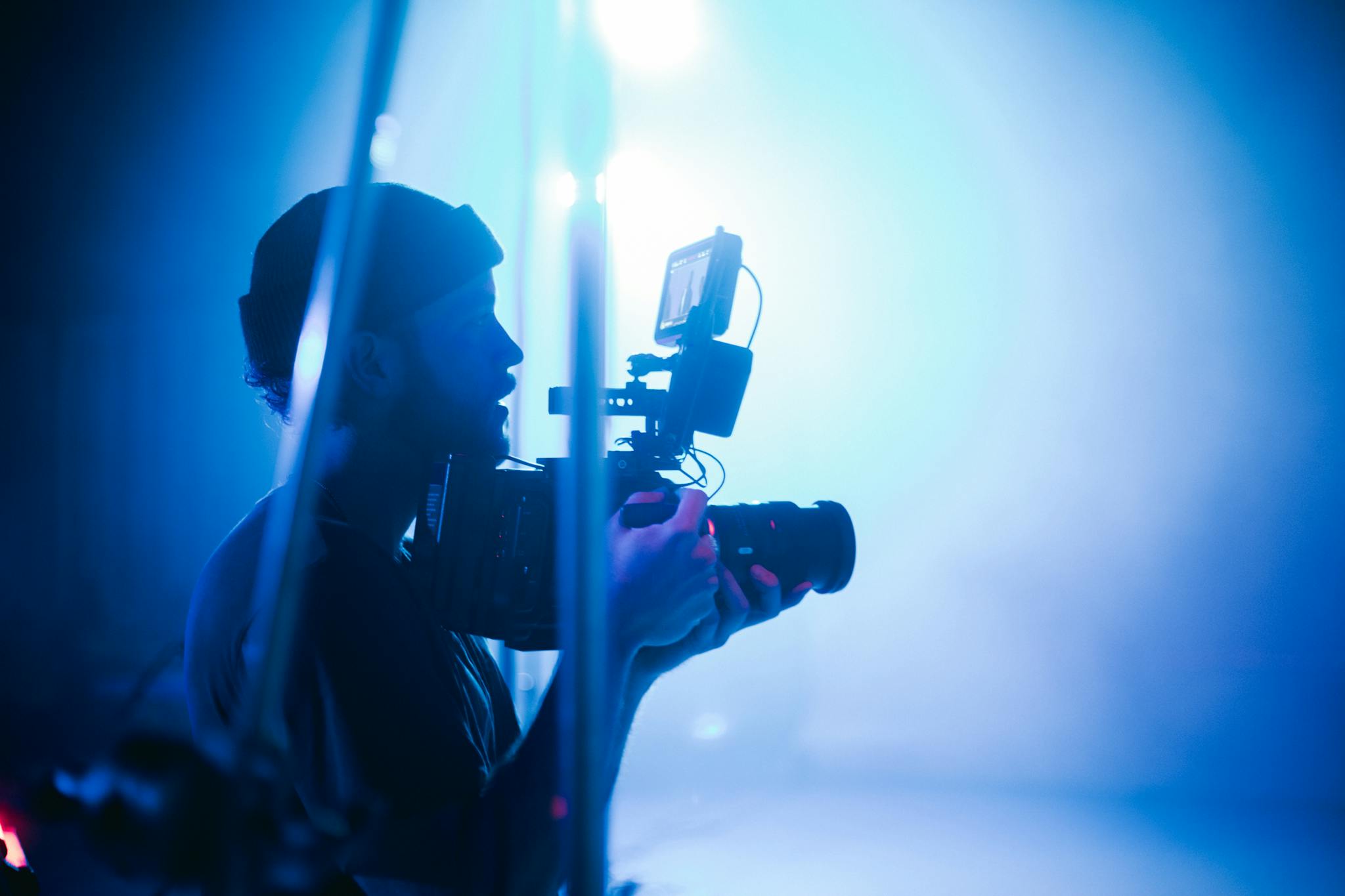Silhouette of a cinematographer using camera equipment in a vibrant blue-lit studio.